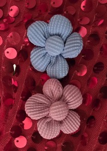 Two fabric flowers, one blue and one pink, placed on a red sequined fabric.